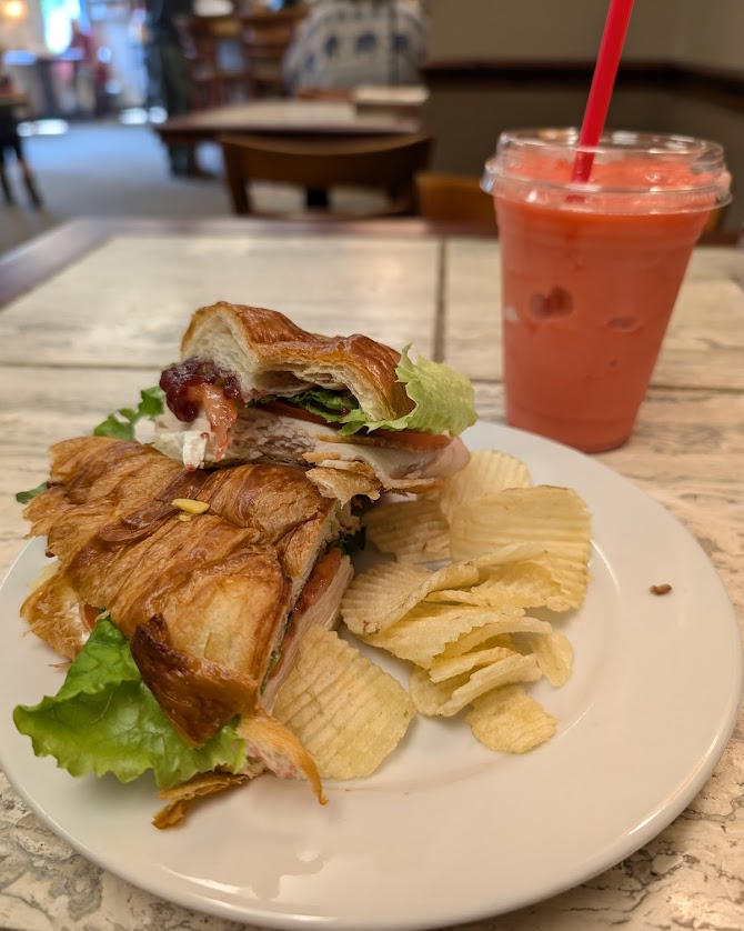 Croissant sandwich loaded with turkey, lettuce, and cranberry sauce, served with chips and a pink drink